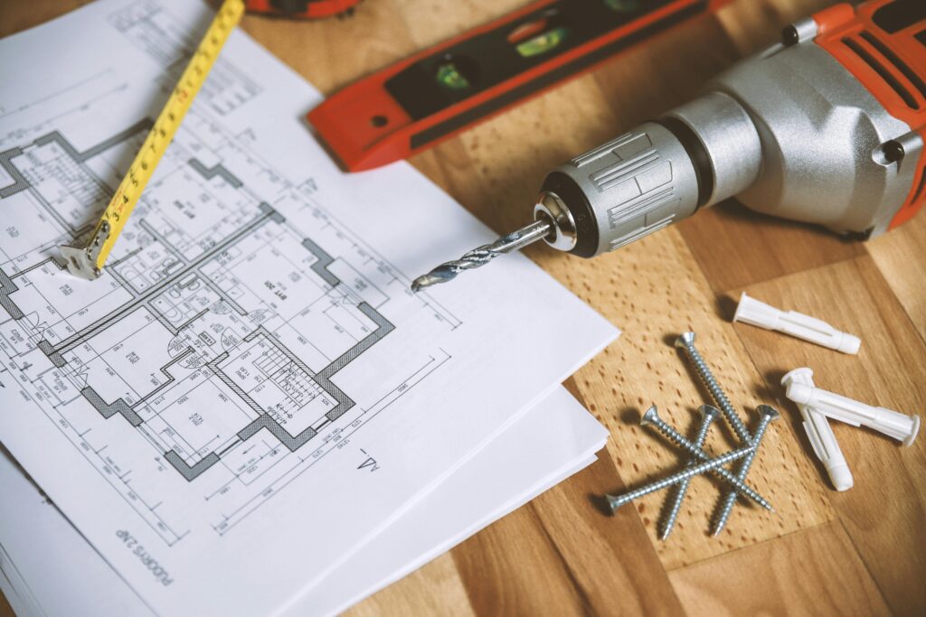 pexels photo 834892 834892 Close-up of construction blueprint with tools like drill and screws on a wooden table.